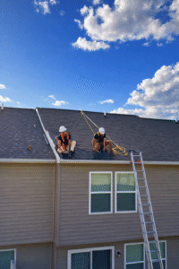 Roofers inspecting storm damage on a West Virginia home roof with safety harnesses and a ladder.