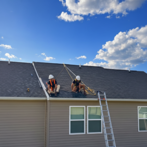 Roofers inspecting storm damage on a West Virginia home roof with safety harnesses and a ladder.
